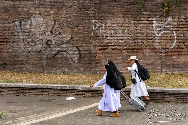 Two nuns walking past an ancient brick wall with graffiti in Rome