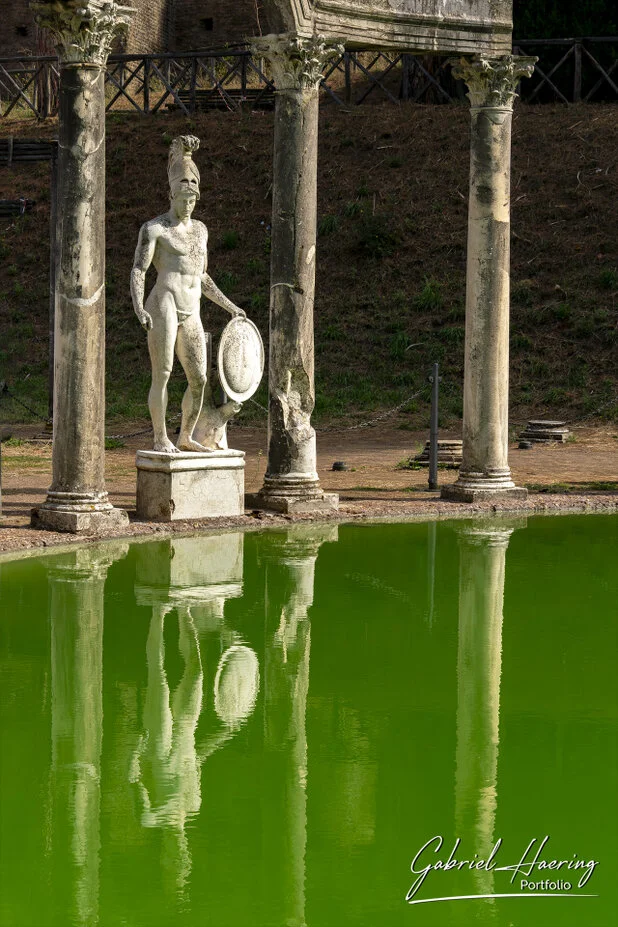 Ancient statue and Roman columns reflected in green water